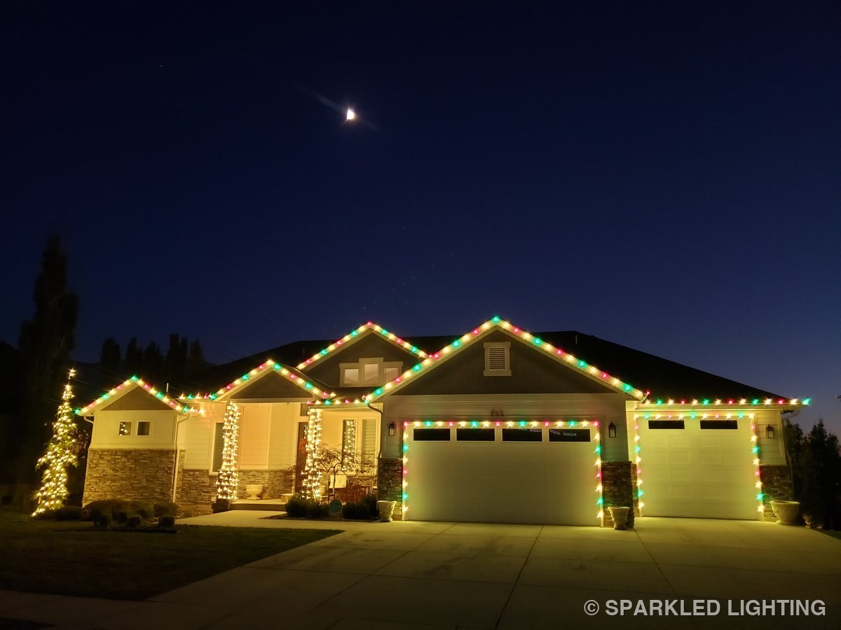A single-story Pleasant View UT home at dusk with Sparkled Lighting seasonal Christmas installation in classic red, green, and warm white