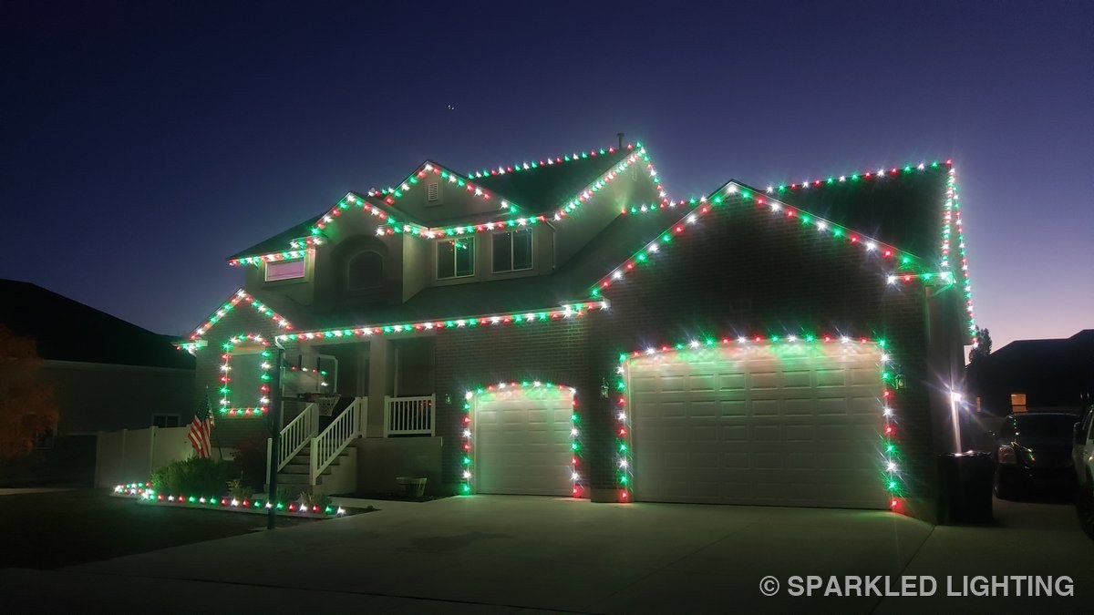 A two-story Syracuse UT home at dusk with Sparkled Lighting seasonal Christmas installation in red, green, and pure white