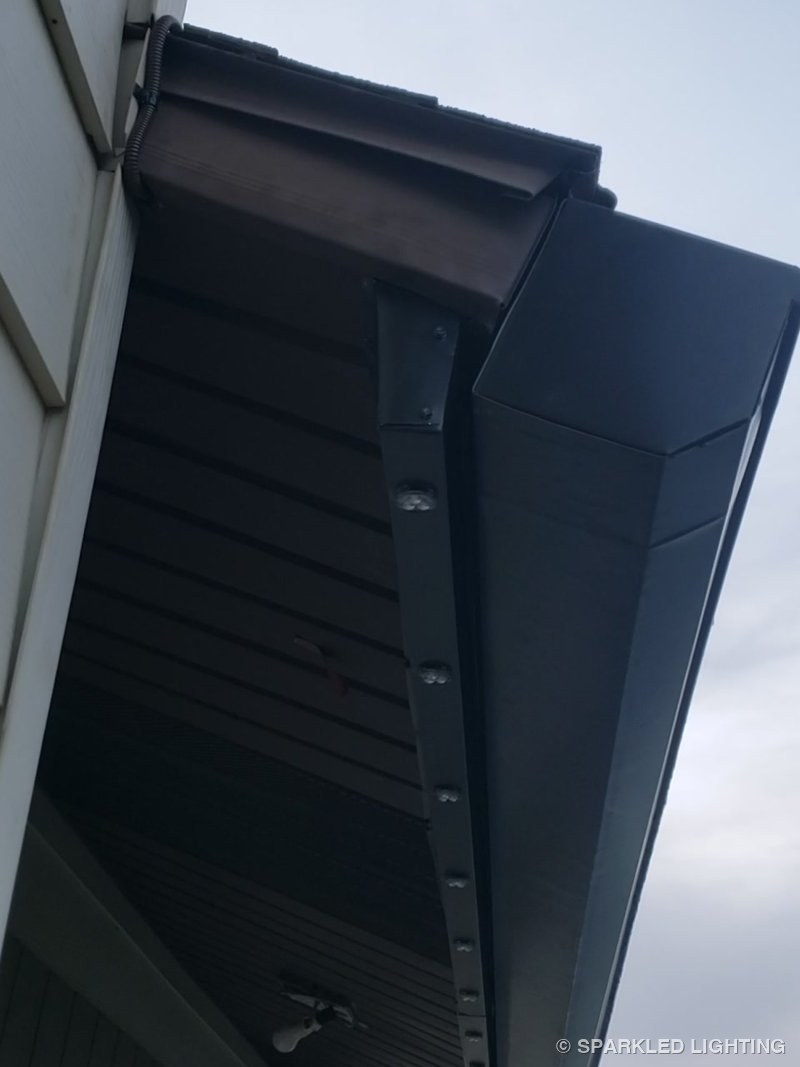 Custom-made channel extending permanent LED lights below an oversized gutter on a Roy Utah garage, by day