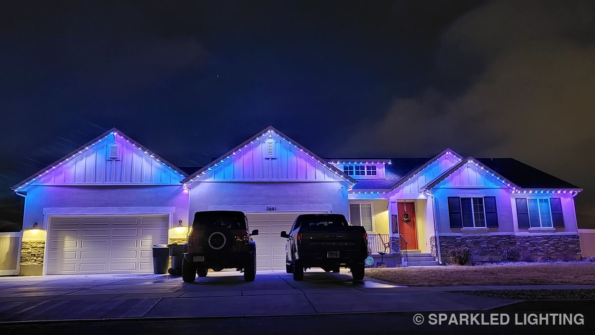 A single-story Clinton UT home at night with Sparkled Lighting permanent LED lights in pink, blue, and white — pastel springtime theme