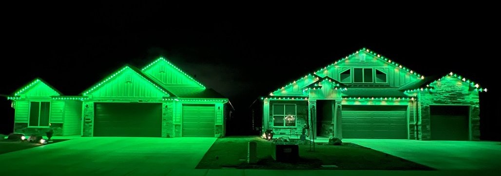 Side-by-side comparison of two homes at night lit in green: the left home is a typical installer's work with bulbs spaced tightly (roughly 6 to 9 inches apart) creating a blurred streak of light along the roofline; the right home is a Sparkled Lighting installation with 12-inch spacing showing each bulb as a distinct, crisp individual point of color