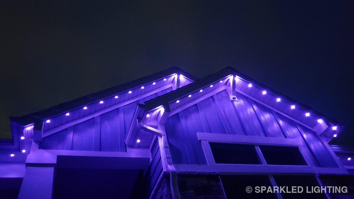 Close-up of permanent LED lights above corbels on a Farr West Utah gable in purple