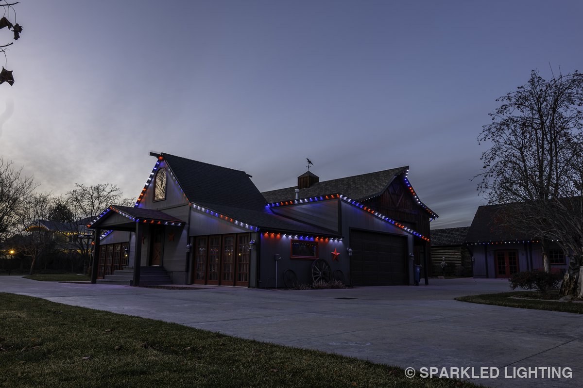 A rural Kaysville UT barn at dusk with Sparkled Lighting permanent LED lights in red, white, and blue — patriotic July 4th display