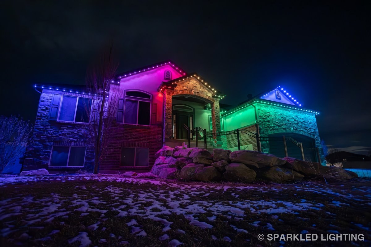 A Syracuse UT home at dusk lit with Sparkled Lighting's permanent LED system showing the full color spectrum — each bulb distinct along the roofline