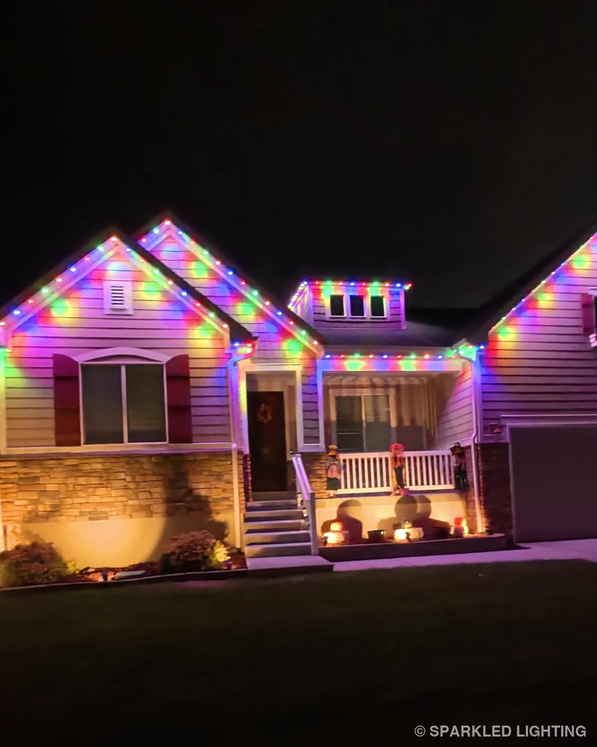 The same Utah home the evening after install, glowing in multicolor permanent LED lights above a pumpkin-lined porch