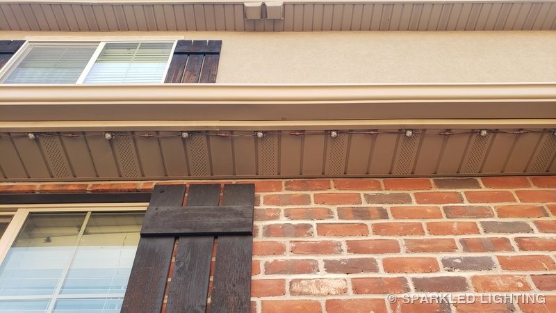 Removable RGBW lights installed on a brown soffit in West Point Utah showing how the color-matched cable disappears against the siding