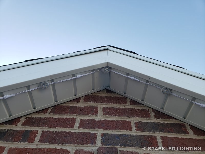Close-up underneath a roof peak showing SmartClip-mounted RGBW pucks and low-profile white cable tucked against a white soffit