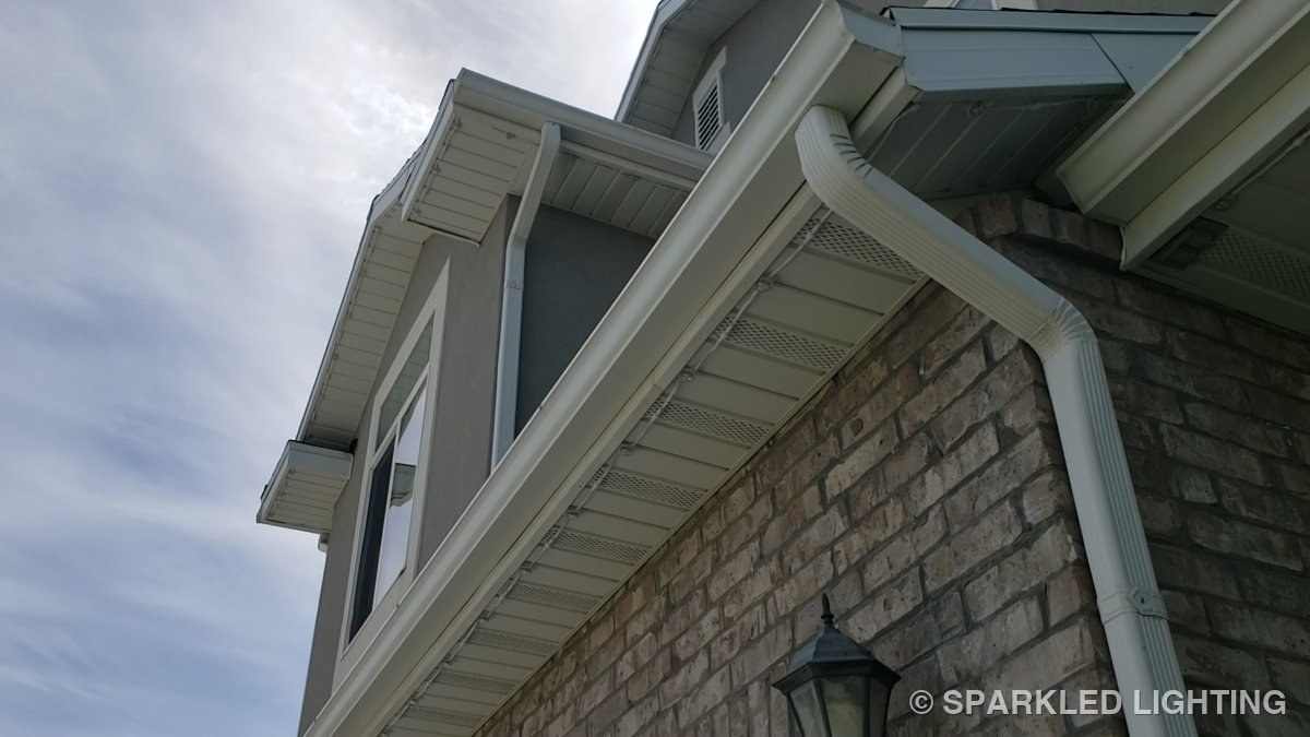 Close-up of SmartClip LED lights under the eave of a Layton Utah home by day, nearly invisible against the white fascia